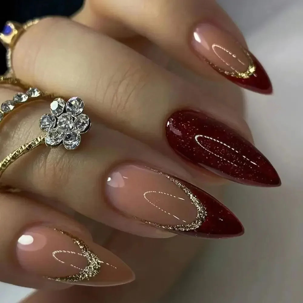 Close-up of a hand displaying long, coffin-shaped press-on false nails with a deep burgundy color and gold glitter accents.