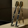 A pair of black toothbrushes with gold accents are shown on a light surface.