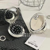 A silver folding massage comb and makeup mirror resting on a black textured surface.