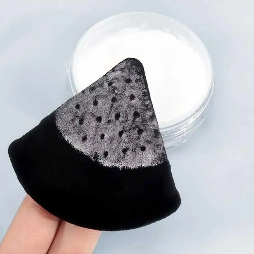 A black triangular velvet powder puff with silver glitter dots is shown next to a clear container of white powder.