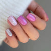 A hand displays a set of pink and purple glossy press-on false nails on fingers against a soft white background.