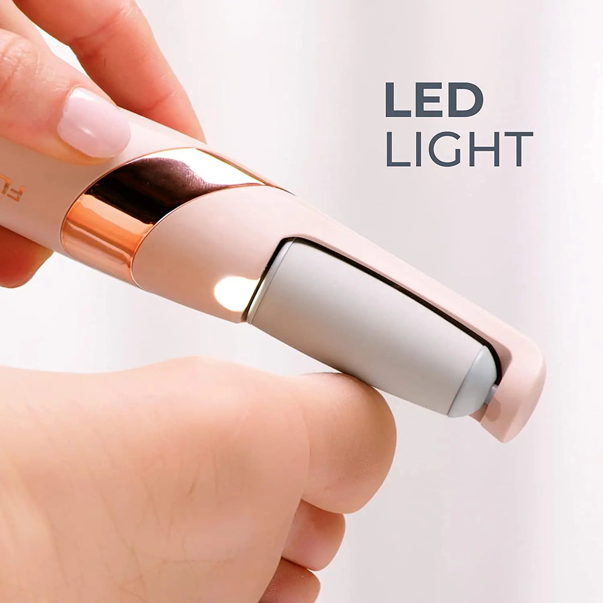 Une main tient un appareil électrique pour les pieds rose et or rose.