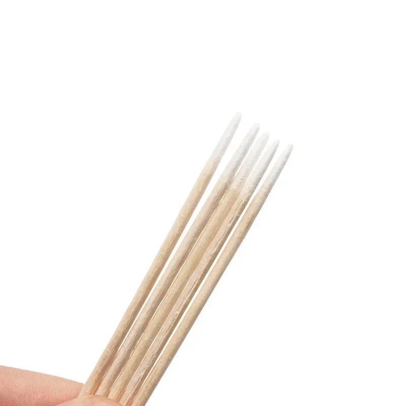 Una mano sostiene un haz de palillos de madera para detalle y cuidado de cutículas.