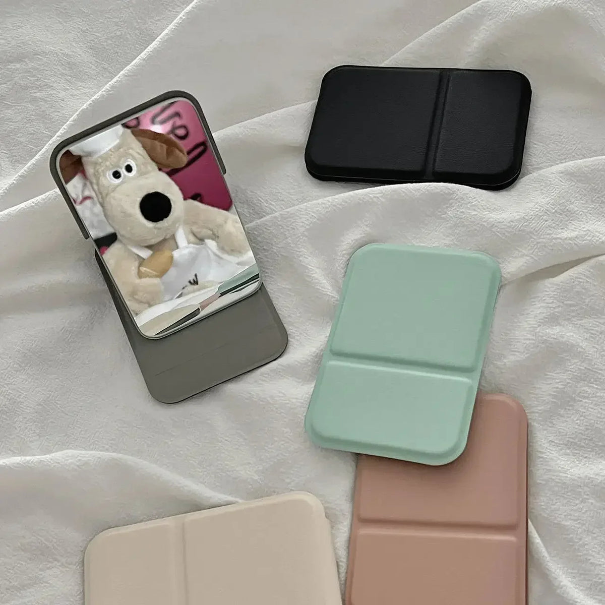 A portable makeup mirror featuring a stuffed dog, shown in various pastel colors and black.
