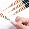 A hand holds a set of professional double-ended nail art brushes with gold and black bristles.