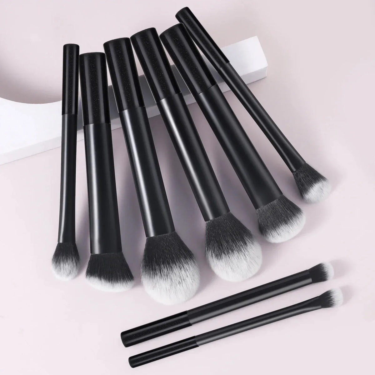A set of nine black and white makeup brushes displayed on a light background.