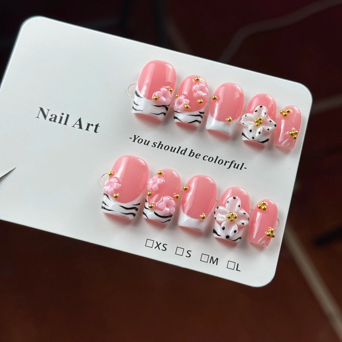 A display of hand-painted pink resin nail art designs in various sizes and shapes with gold accents.