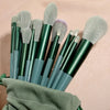 A set of professional makeup brushes with varying sizes and colors stored in a green fabric pouch.