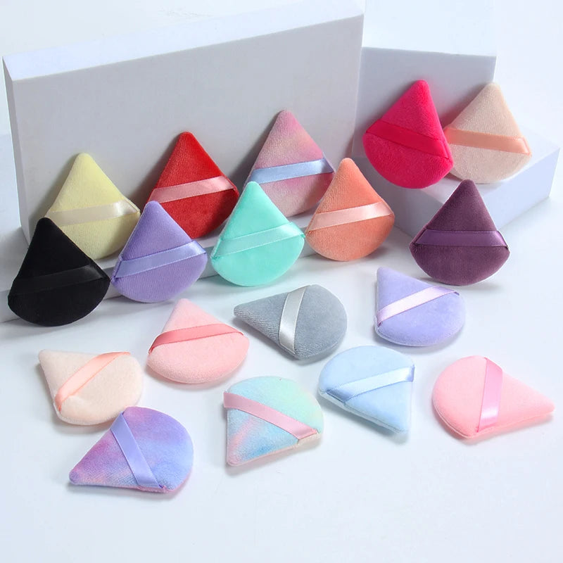 Un set de six éponges de maquillage triangulaires dans différentes nuances de rose, violet et vert sont présentées sur un fon