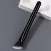 A black triangular precision concealer brush resting on a white cosmetic palette.