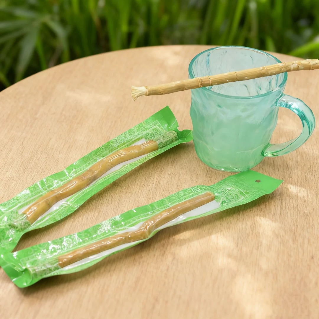 Une tasse en verre et des cure-dents miswak naturels enveloppés dans du matériel vert sont présentés sur une surface en bois.
