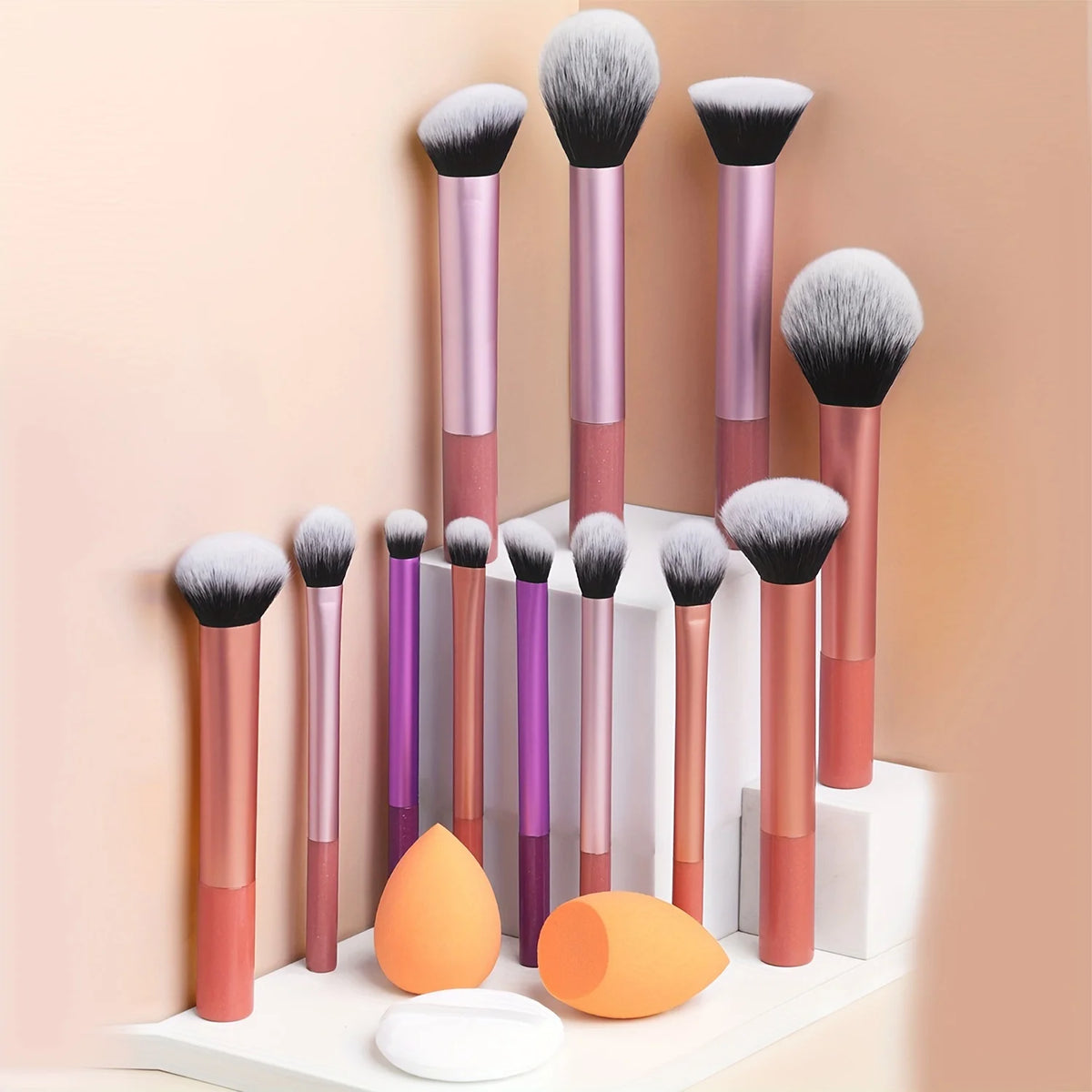 Una colección de doce brochas de maquillaje profesionales en varios tonos de rosa y púrpura sobre una superficie blanca.