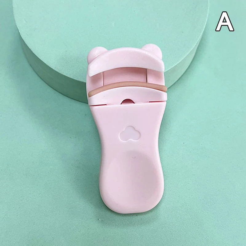 A pink cartoon mini eyelash curler resting on a light green surface.