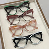 Collection de cinq lunettes à œil de chat pour la lecture, dans différentes nuances de brun, vert et noir, posées sur un tiss