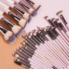 A collection of professional makeup brushes in various shades and sizes laid out on a pink background.