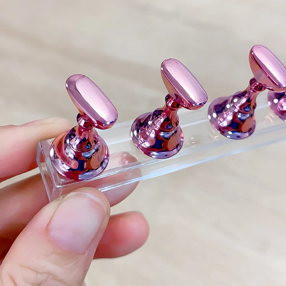 Une main tient un support à ongles en acrylique transparent avec des ongles magnétiques roses métalliques.