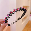 A black rhinestone wave headband decorated with colorful gems, held by a hand.