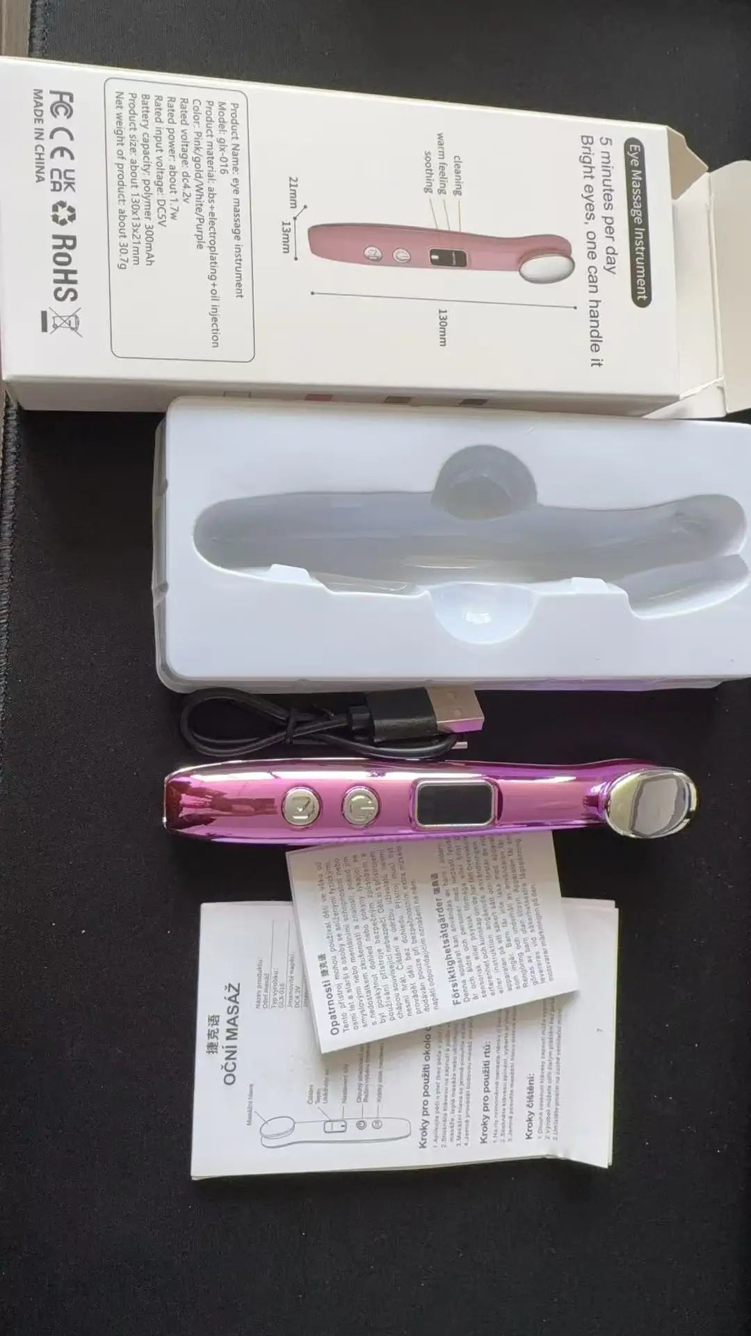 A pink eye massager wand is shown next to its packaging and instructions.