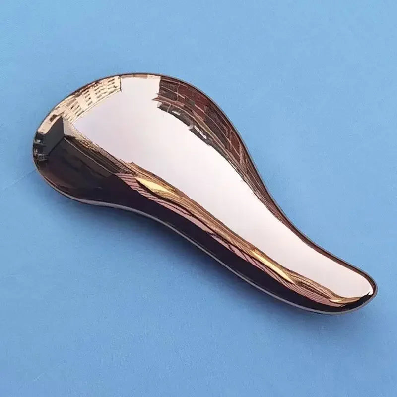 A close-up view of a metallic, curved hair brush with a reflective gold finish against a light blue background.