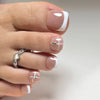 Eine Hand zeigt eine Nageldesign mit sanfter Nude-Basis, weißen French-Tips und zarten silbernen Stud-Akzenten.