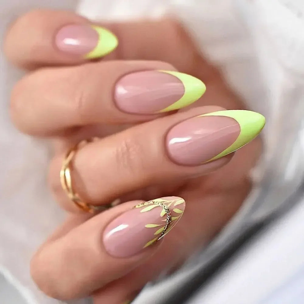 A hand displays press-on false nails with a nude base and yellow-green wavy accents on the tips.