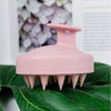 A pink wet and dry scalp massage brush resting on a green leaf.