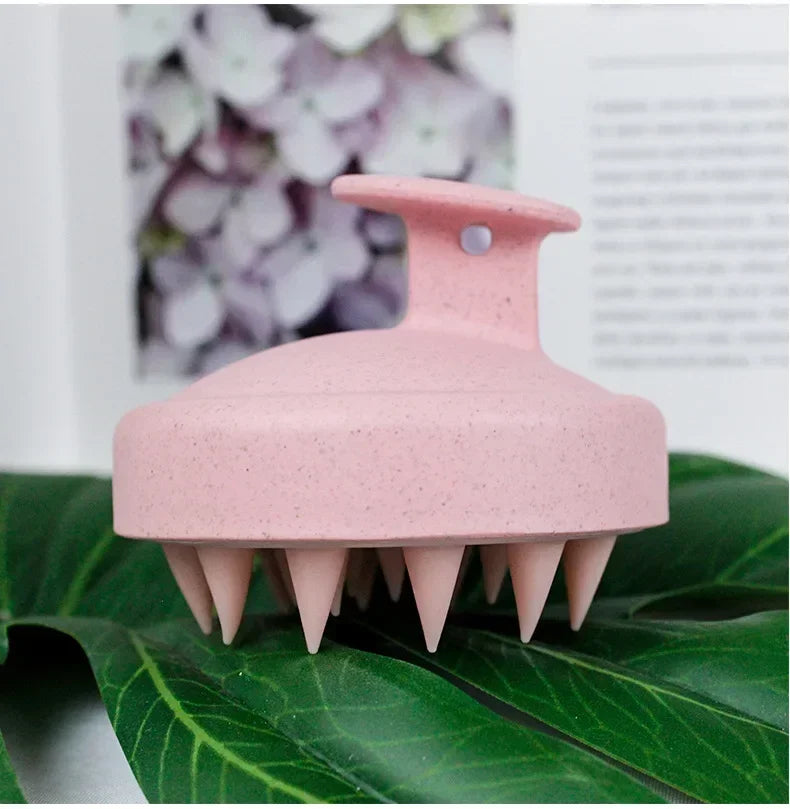 A pink wet and dry scalp massage brush resting on a green leaf.