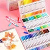 A collection of dual-head art markers in various colors is displayed in a box and laid out on pink surfaces.