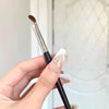 A hand holds a professional angled makeup brush with a silver ferrule and black handle.