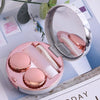 A round pink contact lens storage box with a lid open, showing a clear lens and a white case inside.