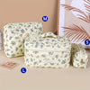 A set of quilted cotton makeup bags in cream and blue floral patterns, including a large pouch, a small pouch, and a rectangu