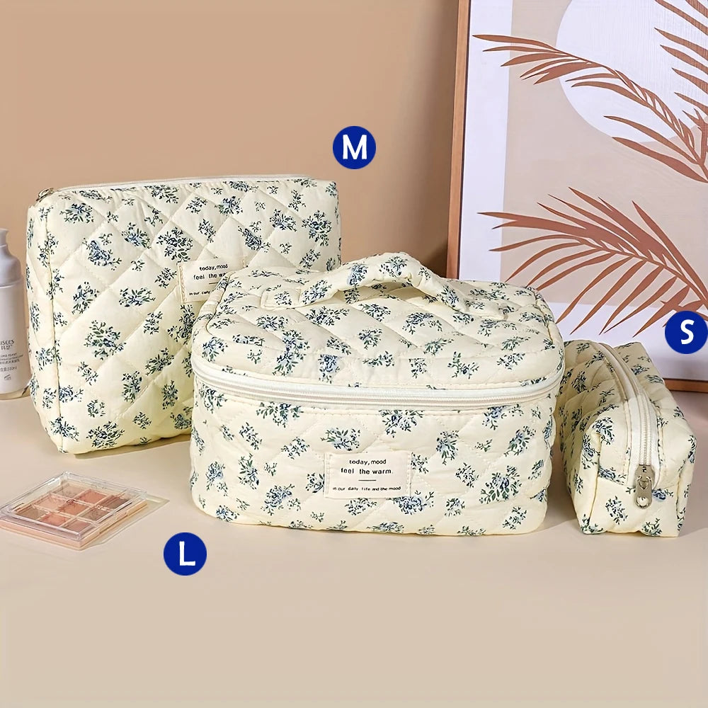 A set of quilted cotton makeup bags in cream and blue floral patterns, including a large pouch, a small pouch, and a rectangu