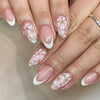 Close-up of hands displaying a press-on acrylic flower nail set with delicate pink and white floral designs