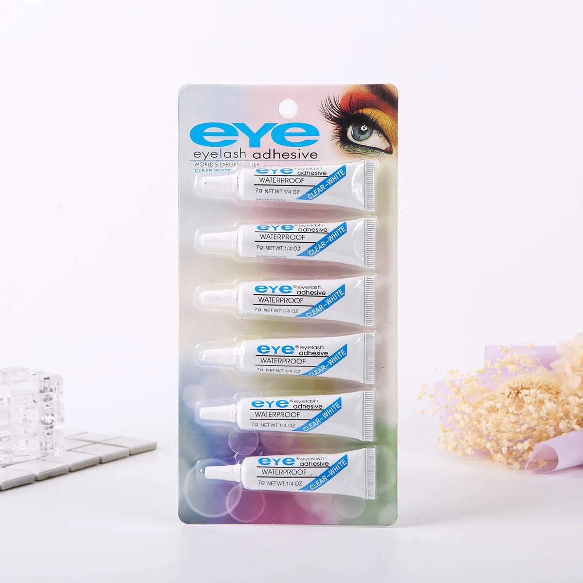 A package of eye adhesive eyelash glue in clear tubes with white caps and a pink background.