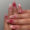 A hand displaying pink heart pearl press-on fake nails with a glossy finish and red accents.