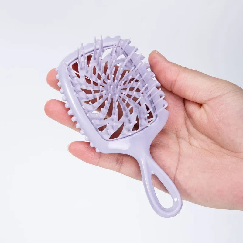 A hand holds a light purple detangling hair comb with a flexible handle.