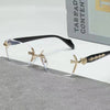 Gold-framed retro frameless reading glasses with clear lenses resting on a gray surface.