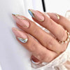A hand displaying press-on false nails with a French wavy design featuring light blue and gold accents.