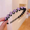 A hand holds a black rhinestone wave headband with purple flowers against a white background.