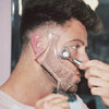 A man is using a beard styling stencil comb on his face to shape his beard.