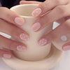 Mains présentant des kits de vernis à ongles fleurs à amande pressées avec un motif pois rose pâle et blanc.