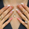 A close-up of hands displaying pink flower press on nails with gold jewelry.
