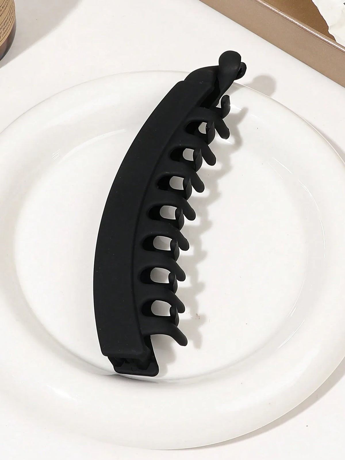 A black banana hair clip is shown resting on a white plate.