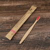 A bamboo toothbrush packaged in natural paper, shown next to a wooden brush.