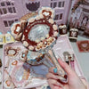 A hand holds a decorative makeup mirror set featuring floral and bear motifs on a pink tray.