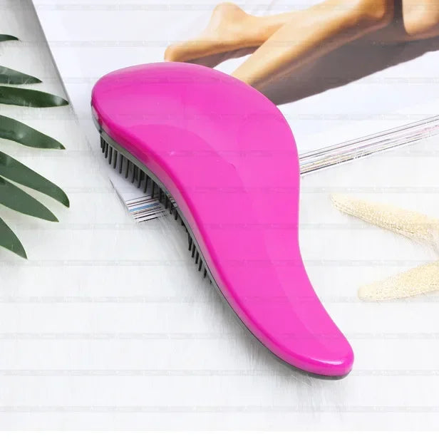 A bright pink classic detangling hair brush lying on a white surface next to a piece of paper and a hand.