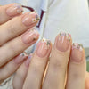 A hand displays a set of press-on acrylic nails decorated with delicate pink and white floral designs.