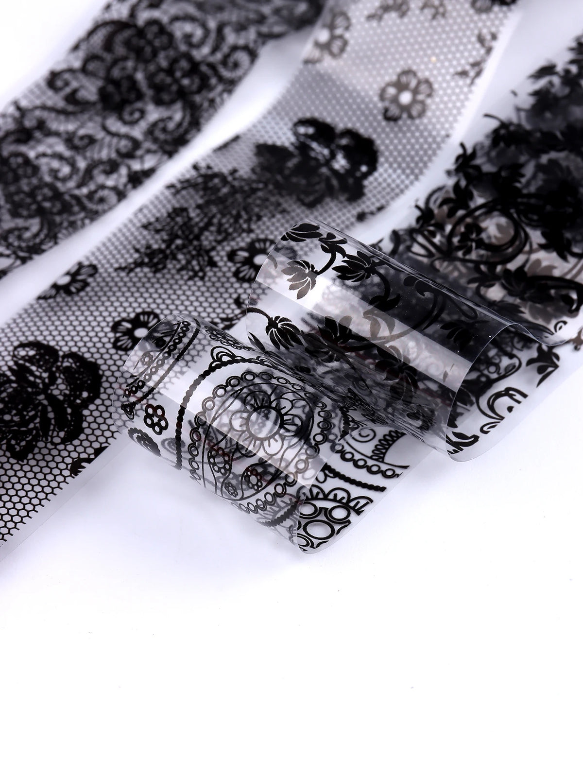 Gros plan de autocollants en feuille translucide à paillettes noir et blanc, montrant des motifs floraux complexes.