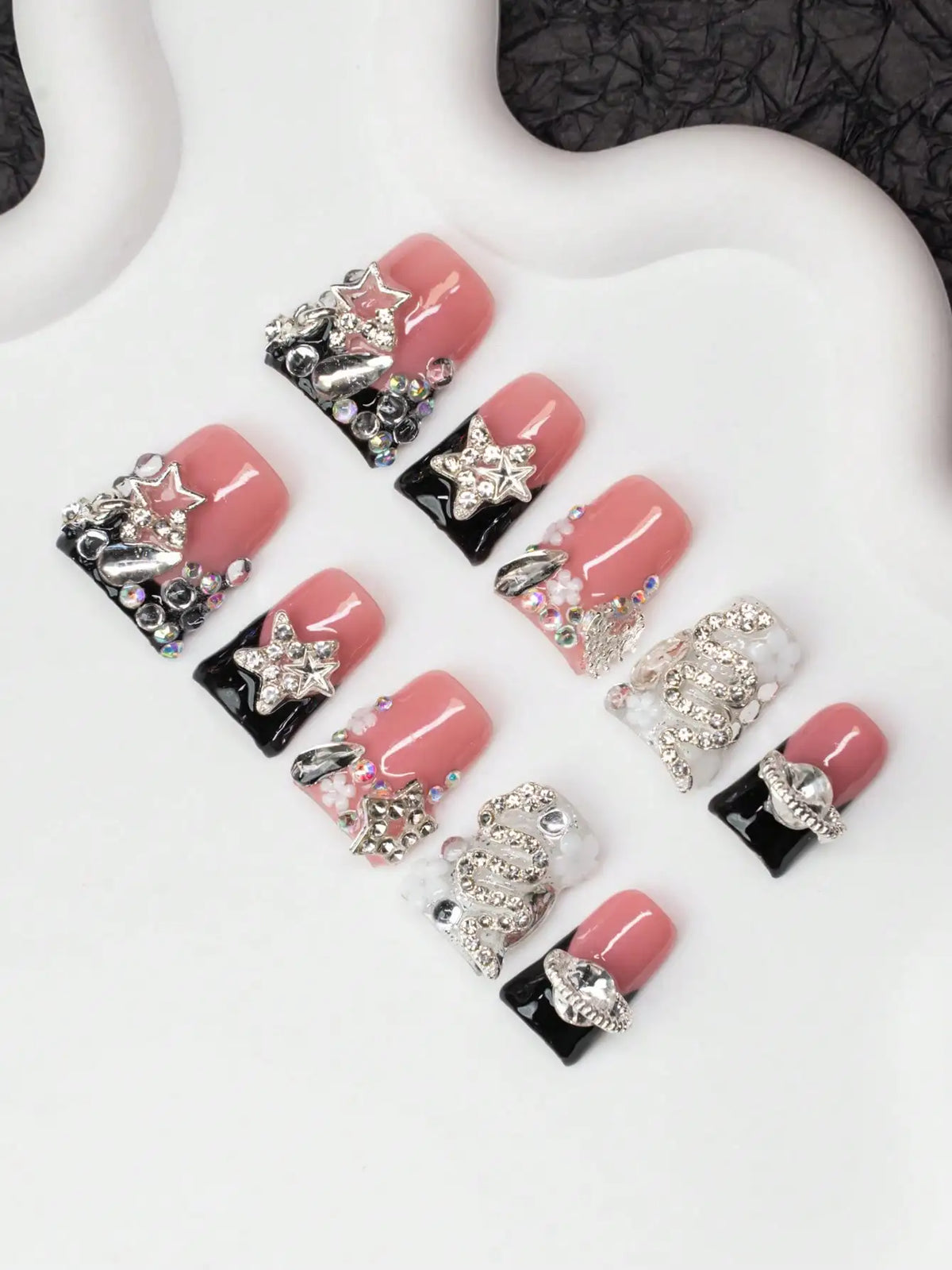 Un set de uñas postizas Y2K con diseños de cristal y estrellas en tonos rosa y negro.