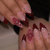 Close-up of a hand displaying 24-piece almond press-on nails with deep red floral and butterfly designs.
